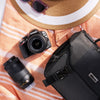 Nikon camera with lens, black bag, and sunglasses on a striped fabric background