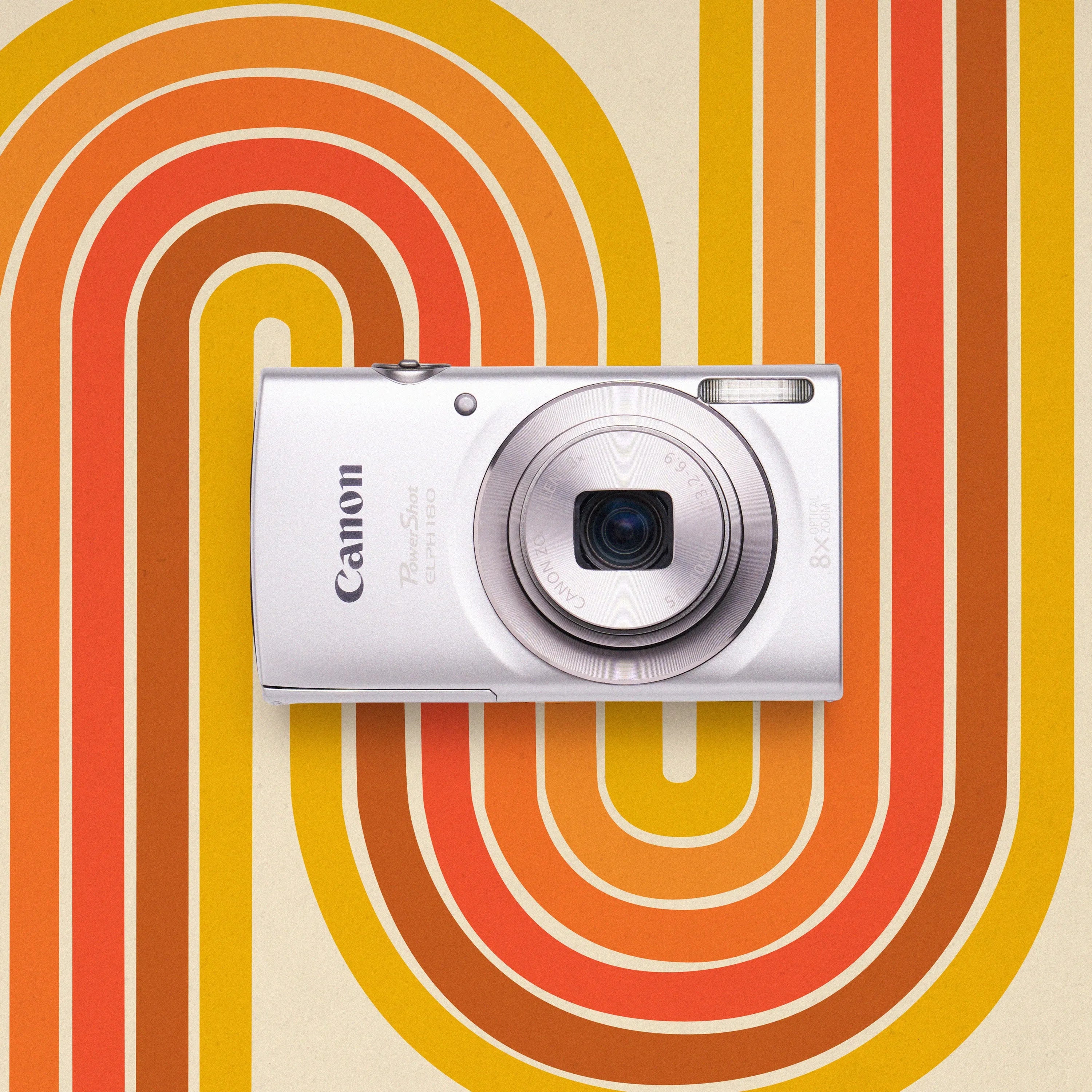 Front view of a silver Canon PowerShot ELPH 180 retro digital camera on an orange and yellow patterned background
