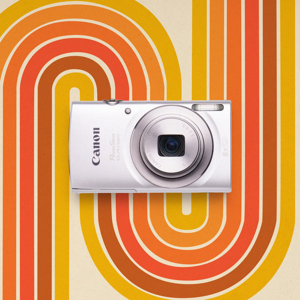 Front view of a silver Canon PowerShot ELPH 180 retro digital camera on an orange and yellow patterned background