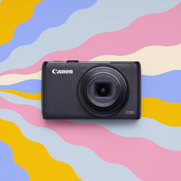 Front view of a restored Canon PowerShot S95 retro digital camera on a colorful wavy background