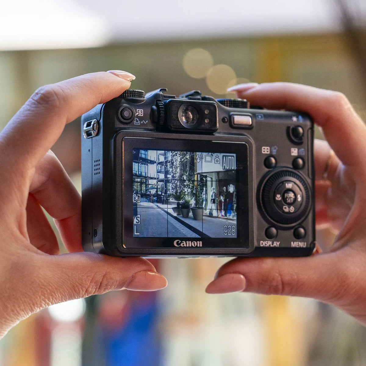 Hands holding a Canon PowerShot G7 with a city scene displayed on its LCD screen