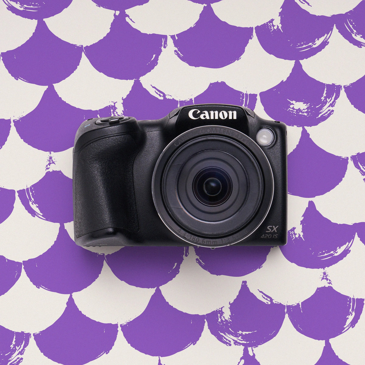 Front view of a restored Canon PowerShot SX420 IS bridge camera on a purple scalloped background