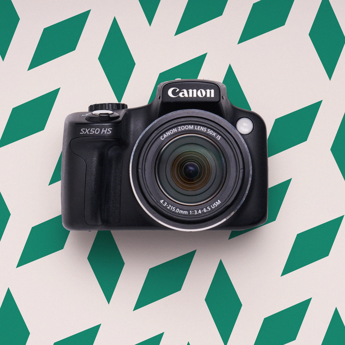 Front view of a black Canon PowerShot SX50 HS digital camera on a green geometric background