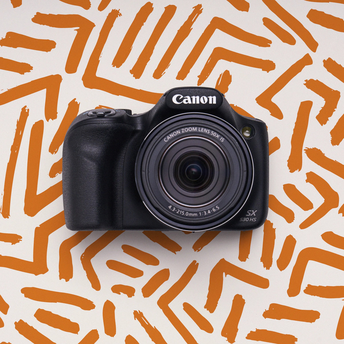 Front view of a restored Canon PowerShot SX530 HS bridge camera on an orange patterned background