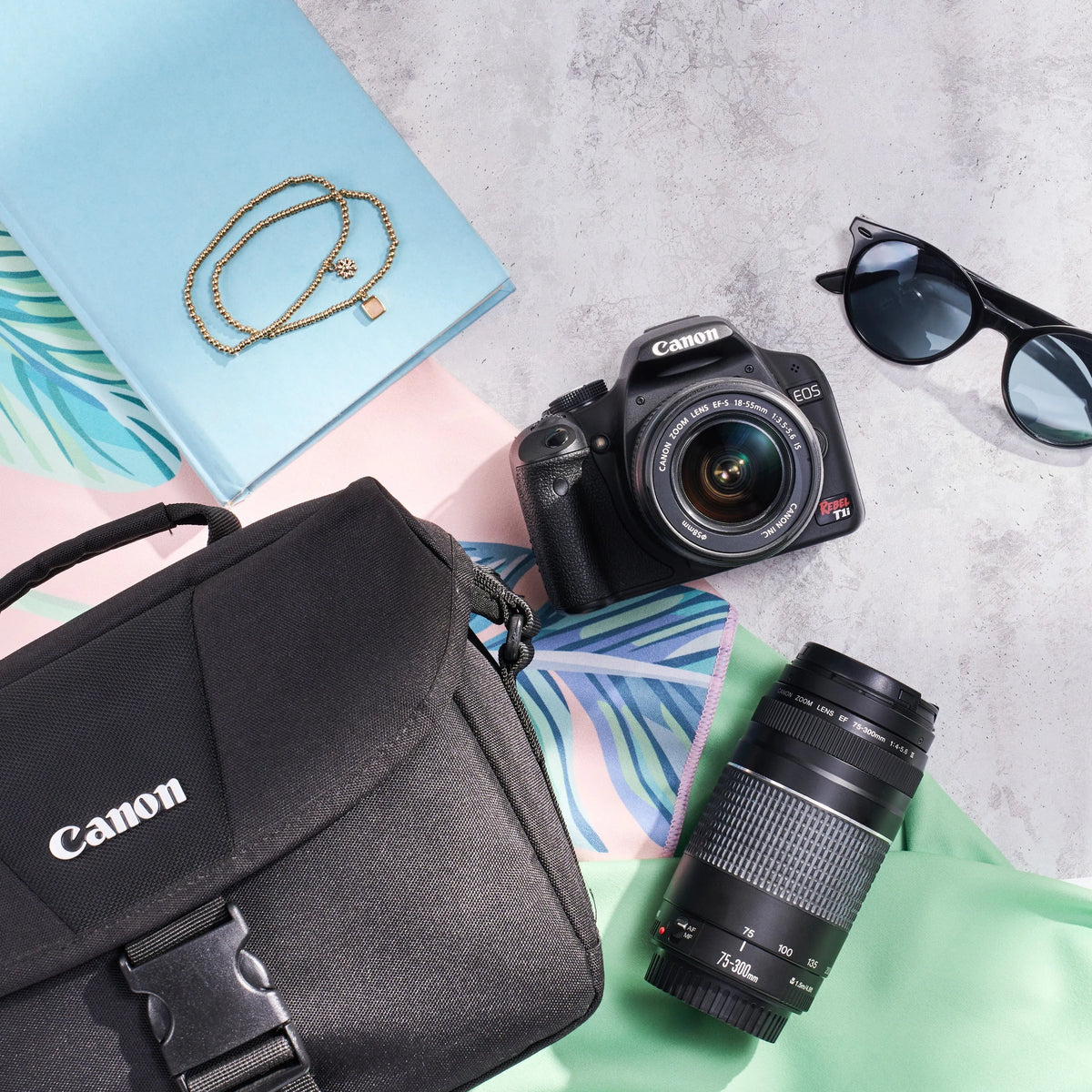 Canon Rebel T1i dual-lens kit arranged with a camera bag, sunglasses and colorful accessories