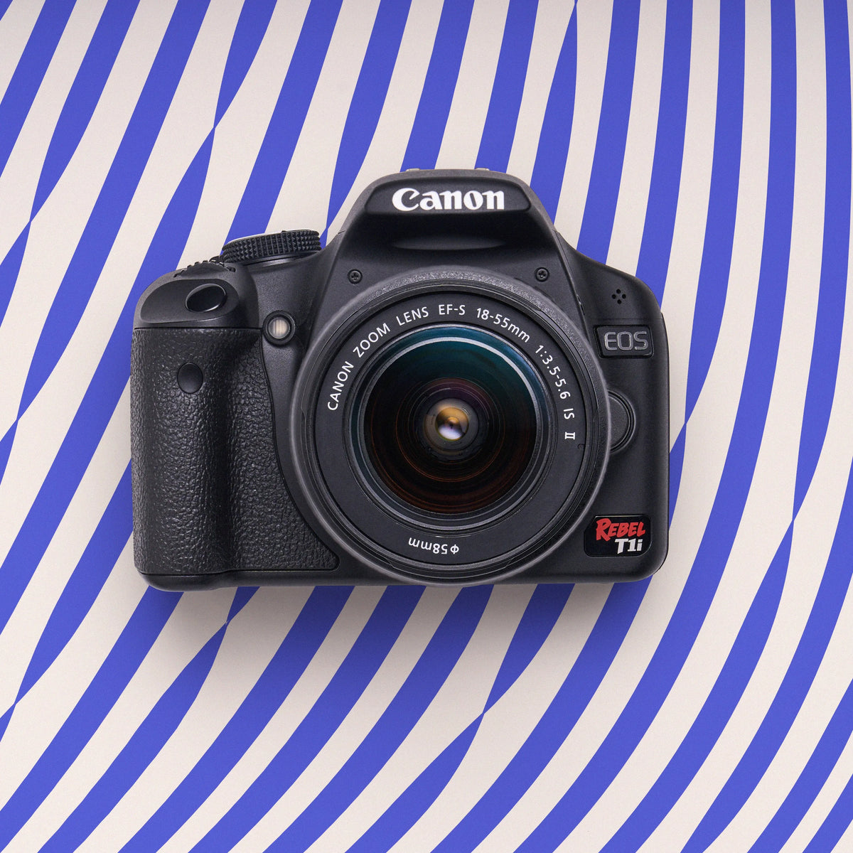 Front view of a restored Canon Rebel T1i DSLR camera with an 18–55mm lens on a purple striped background