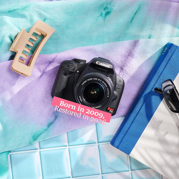 Restored Canon Rebel T1i styled with colorful accessories, labeled Born in 2009, Restored in 2026