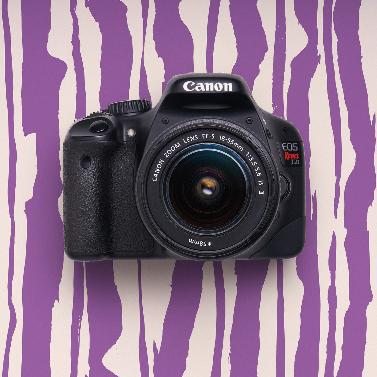 Front view of a restored Canon Rebel T2i DSLR camera with an 18–55mm lens on a purple striped background