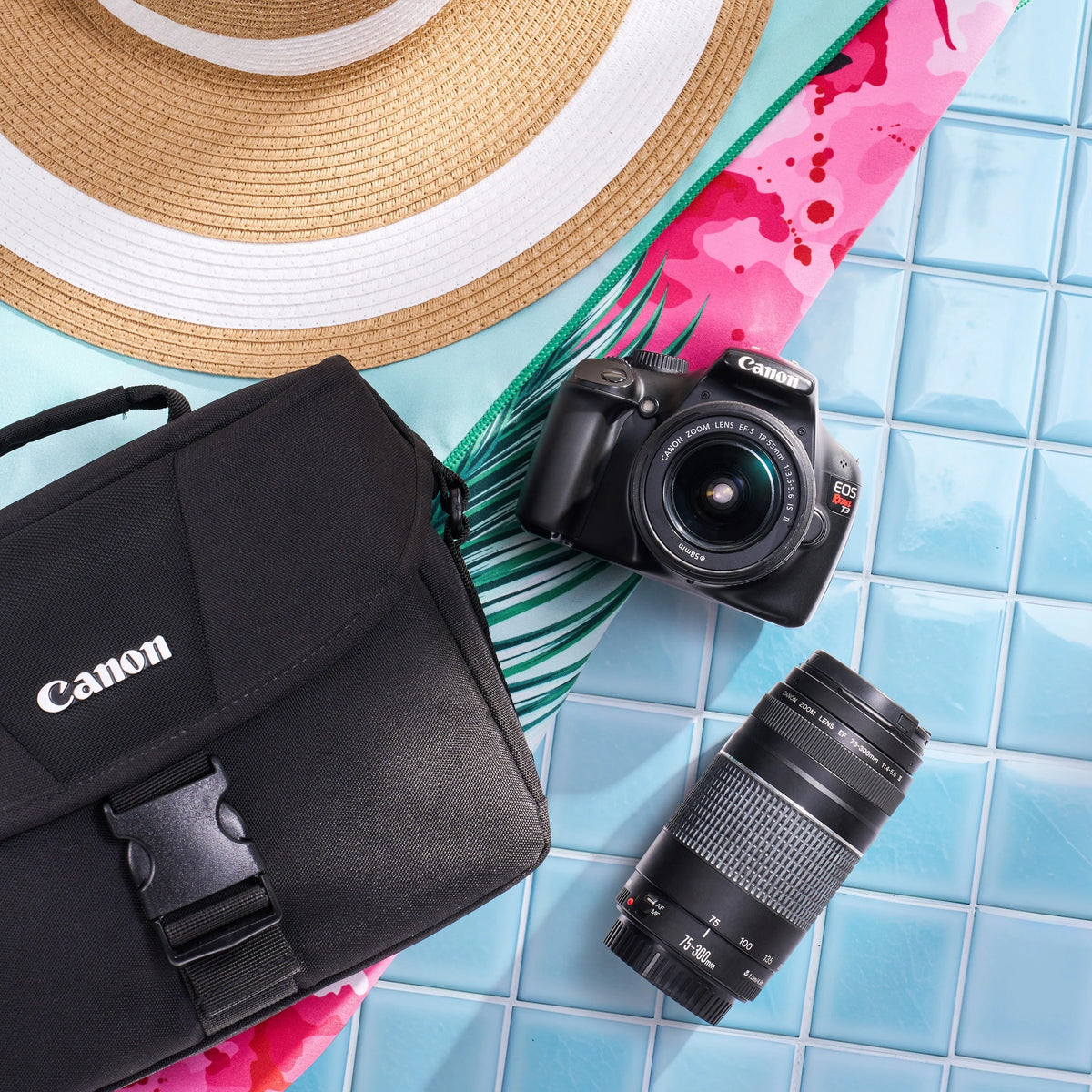 Canon Rebel T3 dual-lens kit arranged with a camera bag, sun hat and colorful accessories