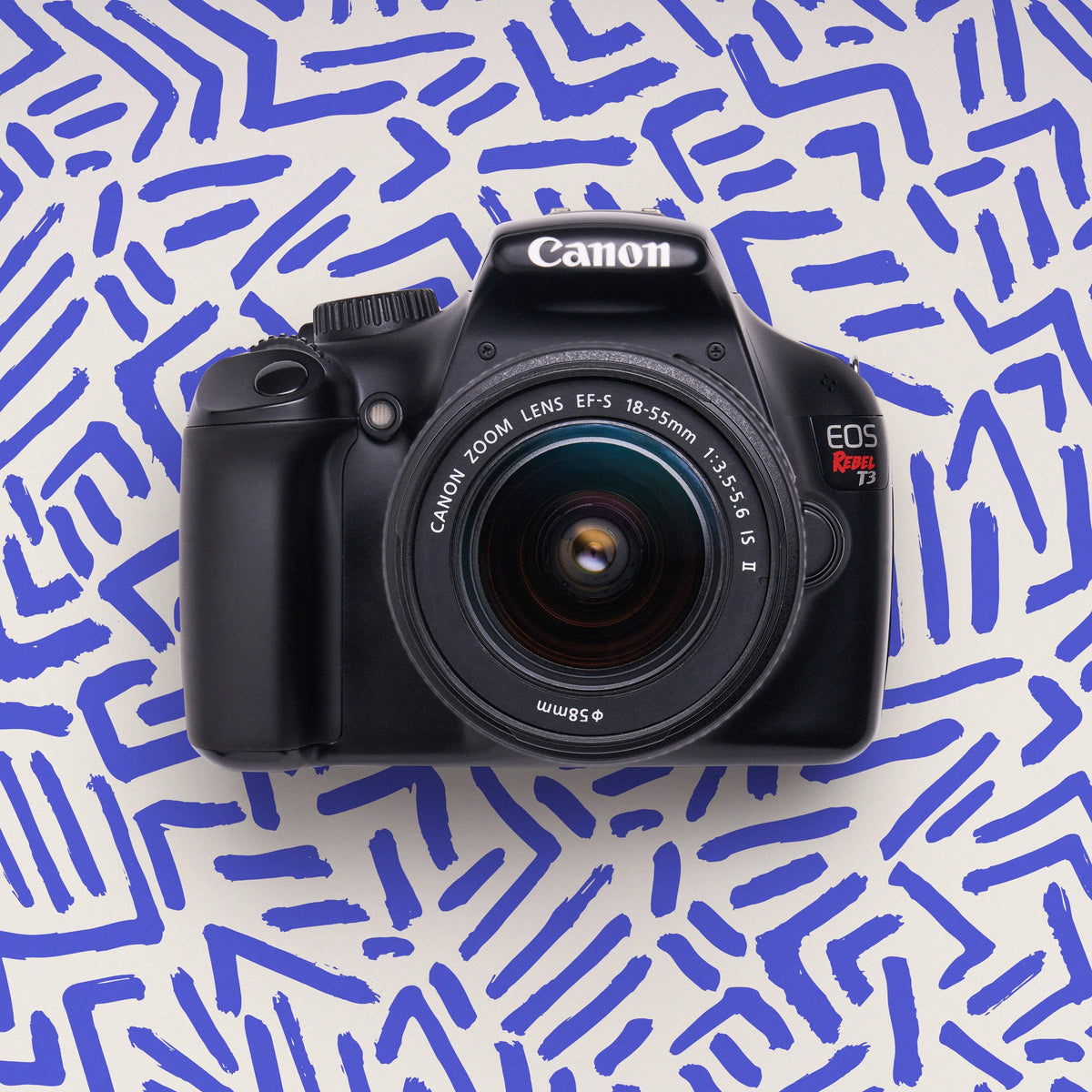 Front view of a restored Canon Rebel T3 DSLR camera with an 18–55mm lens on a blue patterned background
