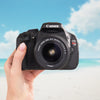 Canon Rebel T3i DSLR camera with an 18–55mm lens held against a beach backdrop
