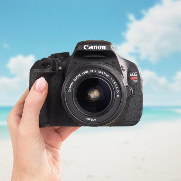 Canon Rebel T3i DSLR camera with an 18–55mm lens held against a beach backdrop
