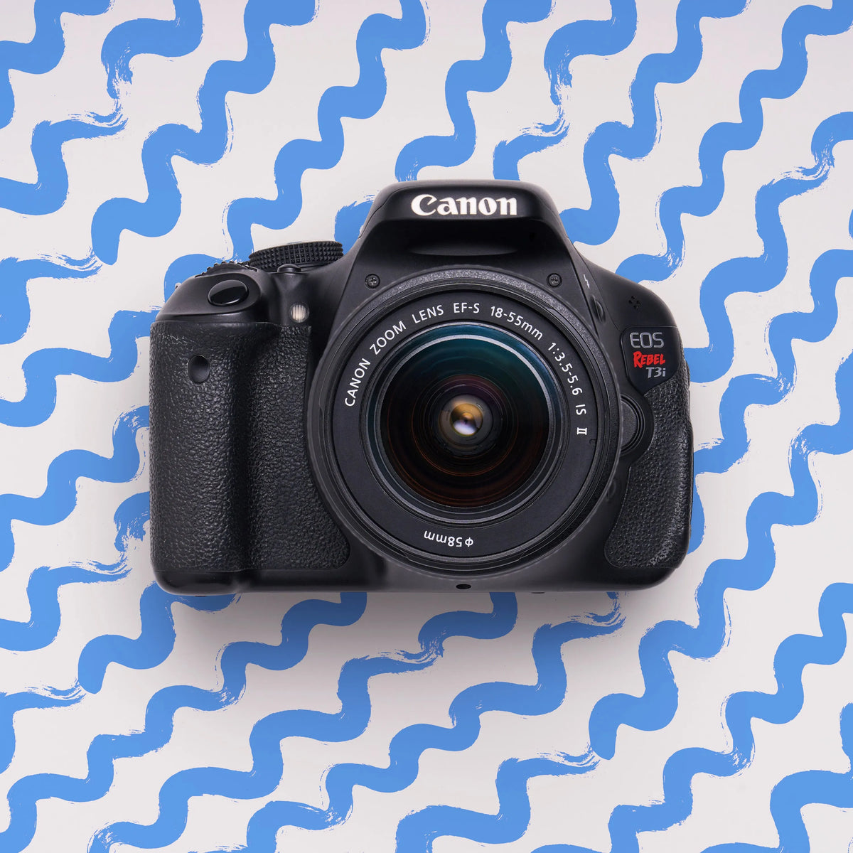 Front view of a restored Canon Rebel T3i DSLR camera with an 18–55mm lens on a blue patterned background
