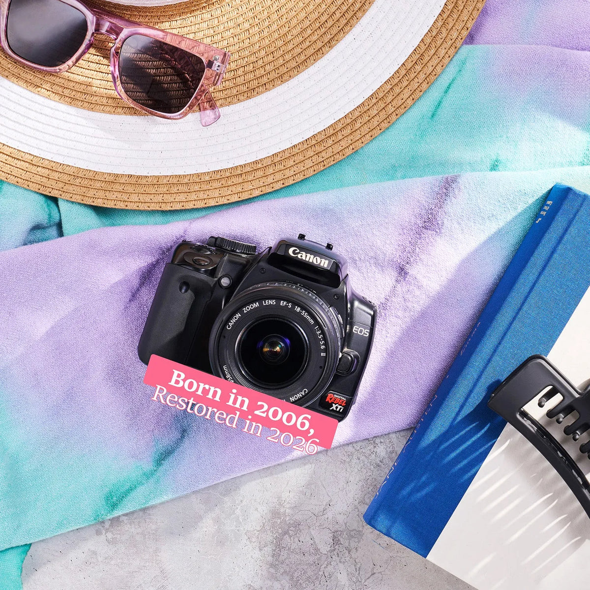 Restored Canon Rebel XTi styled with a sun hat and sunglasses, labeled Born in 2006, Restored in 2026