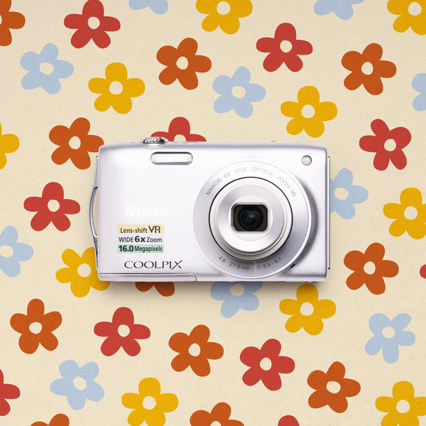 Front view of a silver Nikon COOLPIX S3300 retro digital camera on a colorful flower-patterned background