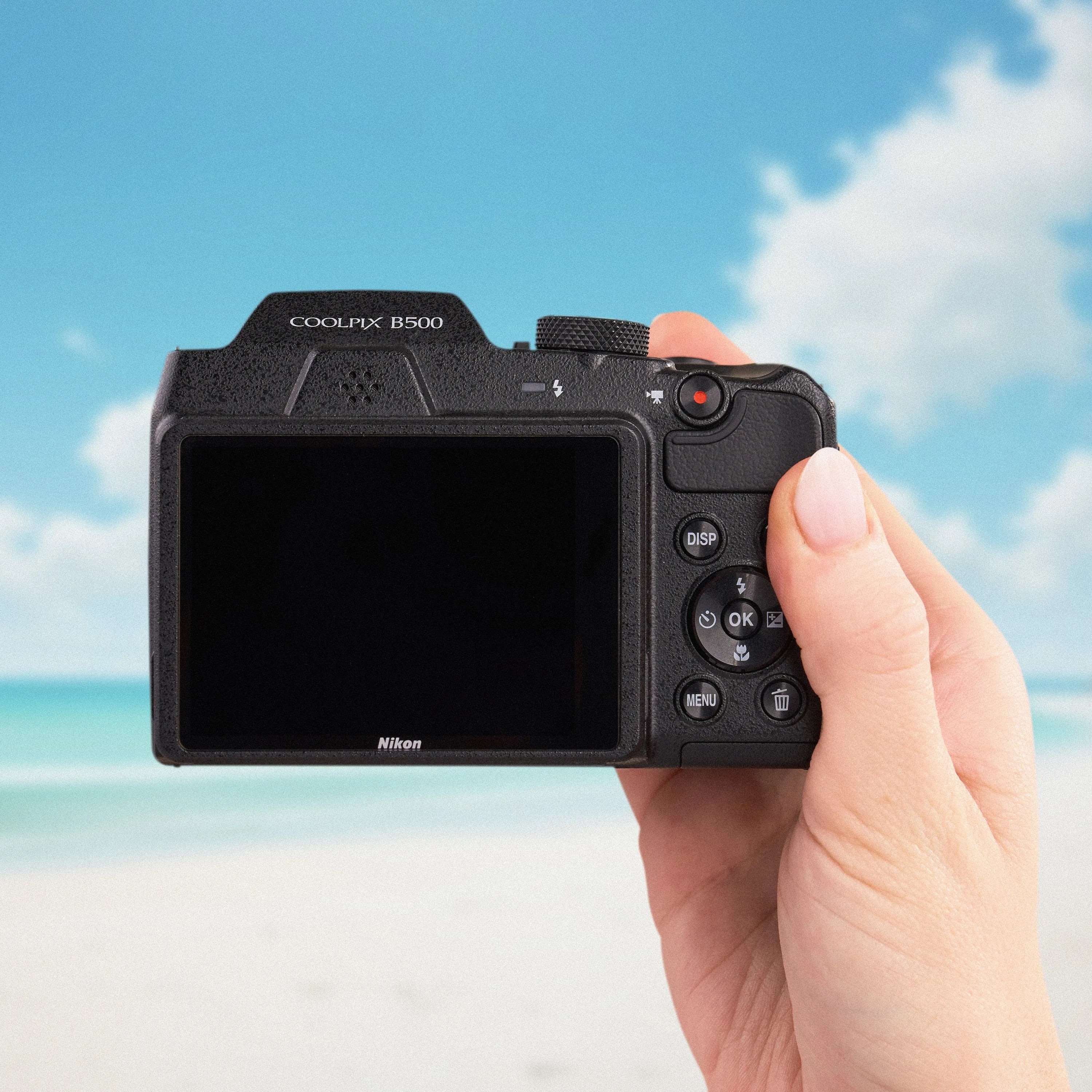 Back view of the Nikon COOLPIX B500 showing its LCD screen and controls against a beach backdrop