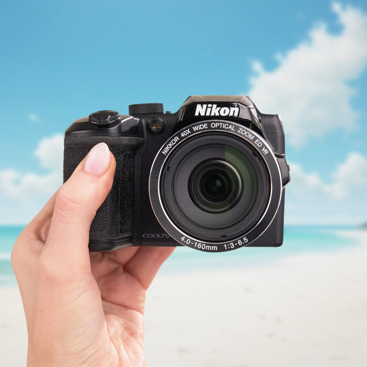 Nikon COOLPIX B500 held from the front with its 40x optical zoom lens against a beach backdrop