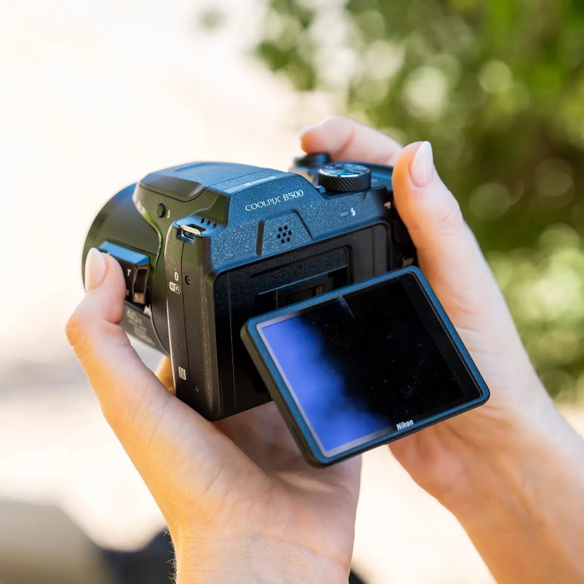 Nikon COOLPIX B500 held outdoors with its tilting LCD screen extended
