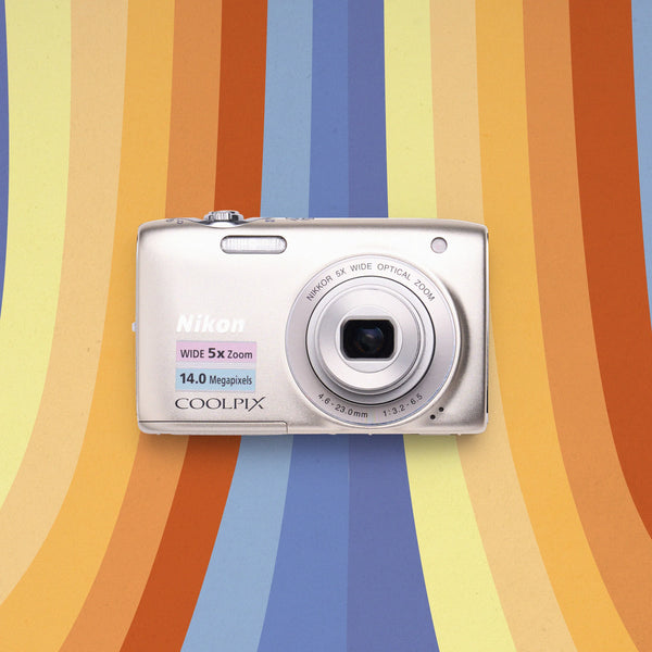 Front view of a silver Nikon COOLPIX S3100 retro digital camera on a colorful striped background
