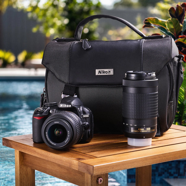 Nikon D3100 dual-lens camera kit with a Nikon bag displayed beside a swimming pool