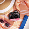 Restored Nikon D3100 styled with beach accessories and text reading “Born in 2010, Restored in 2026”