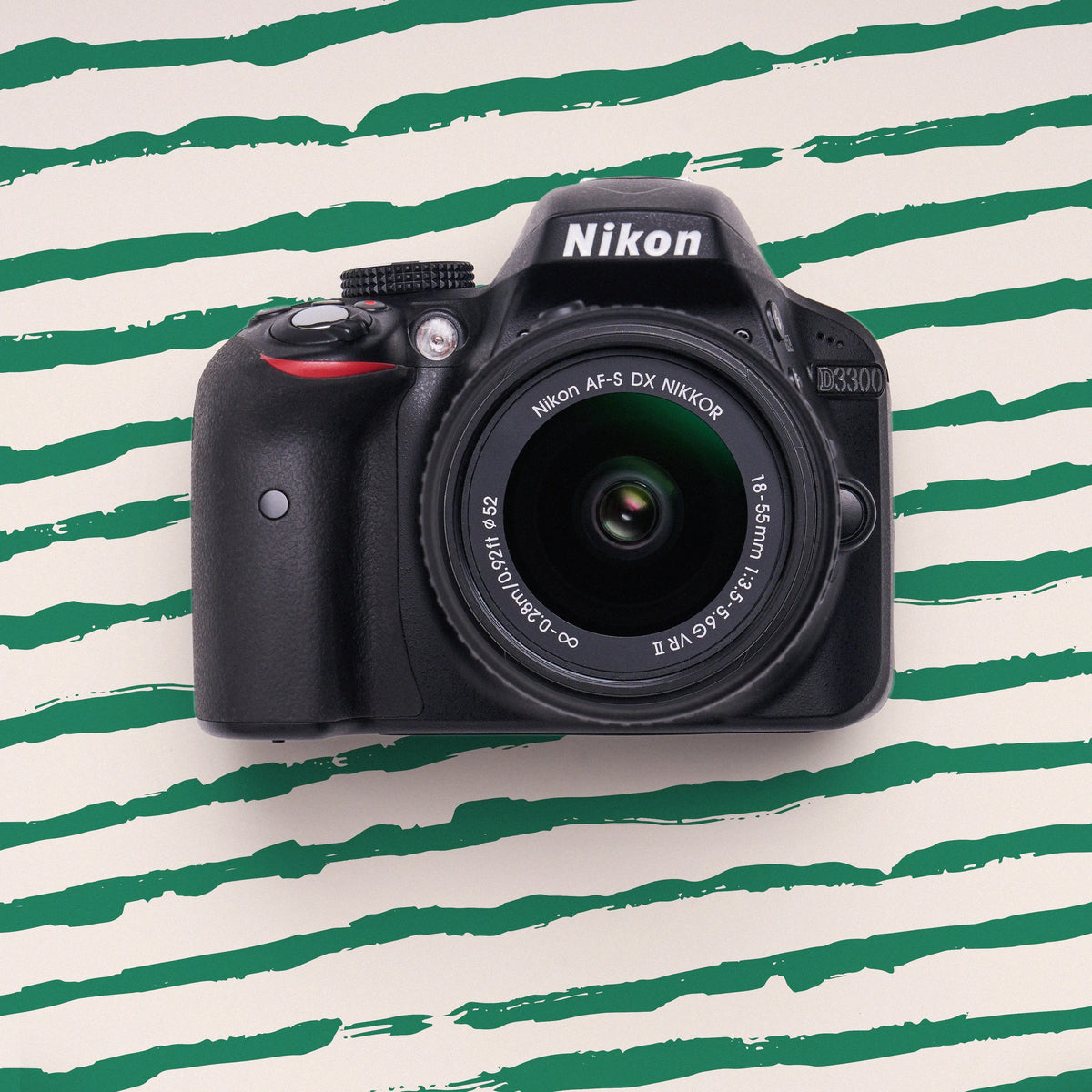 Front view of a Nikon D3300 DSLR with an 18–55mm lens on a green striped background