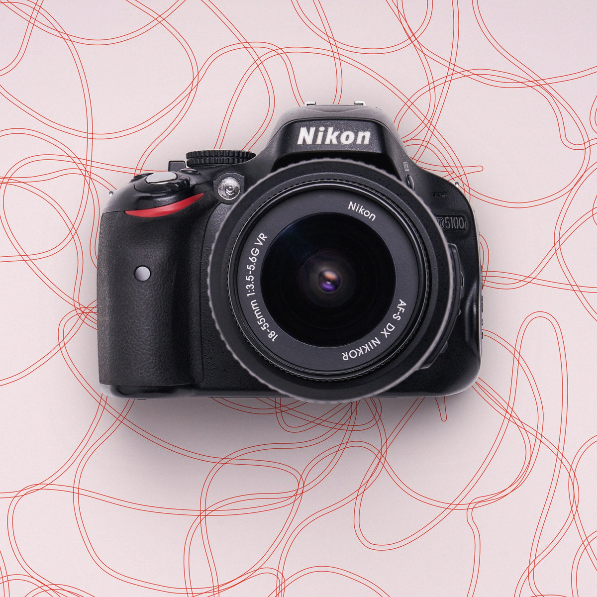 Front view of a restored Nikon D5100 DSLR camera with an 18–55mm lens on a pink abstract background