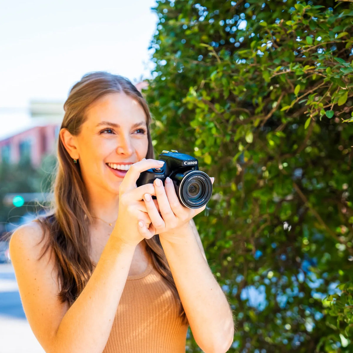 Woman smiling while taking a photograph outdoors with a Canon PowerShot SX50 HS