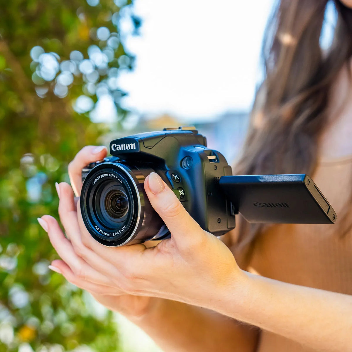 Close-up of a woman holding a Canon PowerShot SX50 HS with its flip-out screen open outdoors
