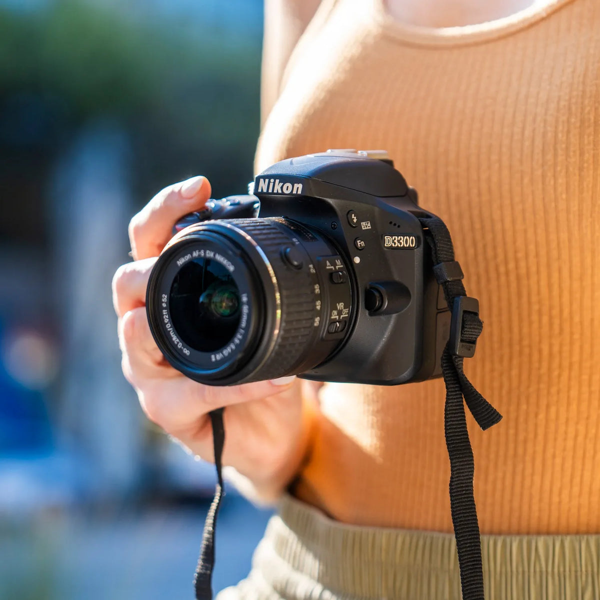 Person holding a Nikon D3300 DSLR with an 18–55mm lens outdoors