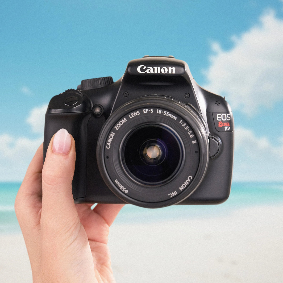 Canon Rebel T3 DSLR camera with an 18–55mm lens held against a beach backdrop