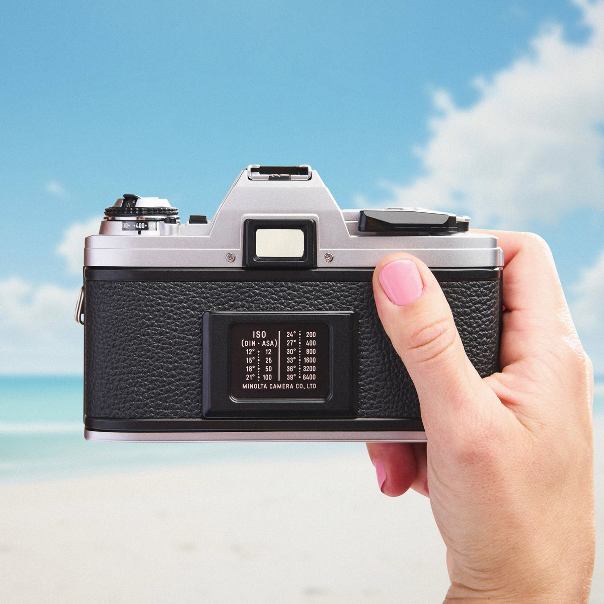 Hand holding a Minolta X-370 35mm film camera with a beach and sky background