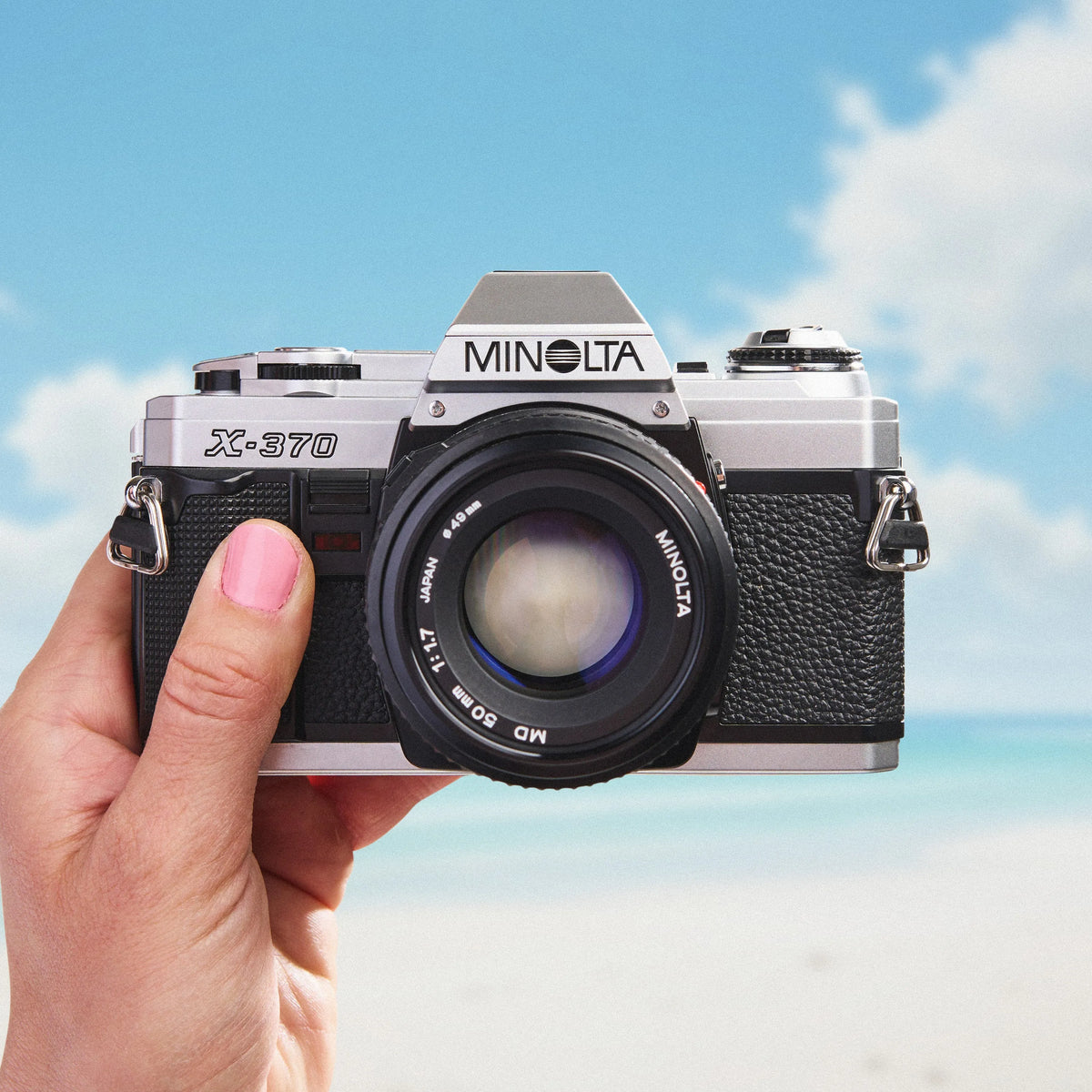 Minolta X-370 35mm film camera  held in a hand with a blue sky background