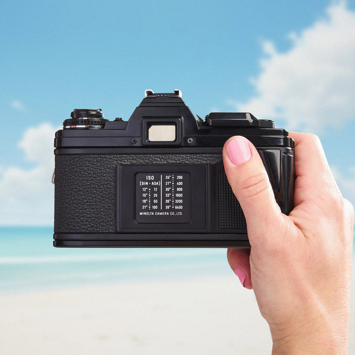 Hand holding a Minolta X-700 | 35mm Film Camera against a blue sky and beach background