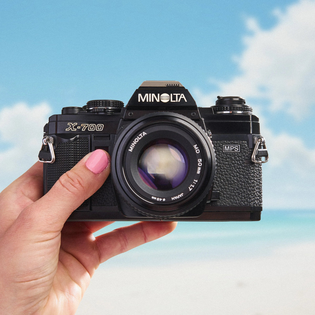 Minolta X-700 camera held in a hand with a blue sky background