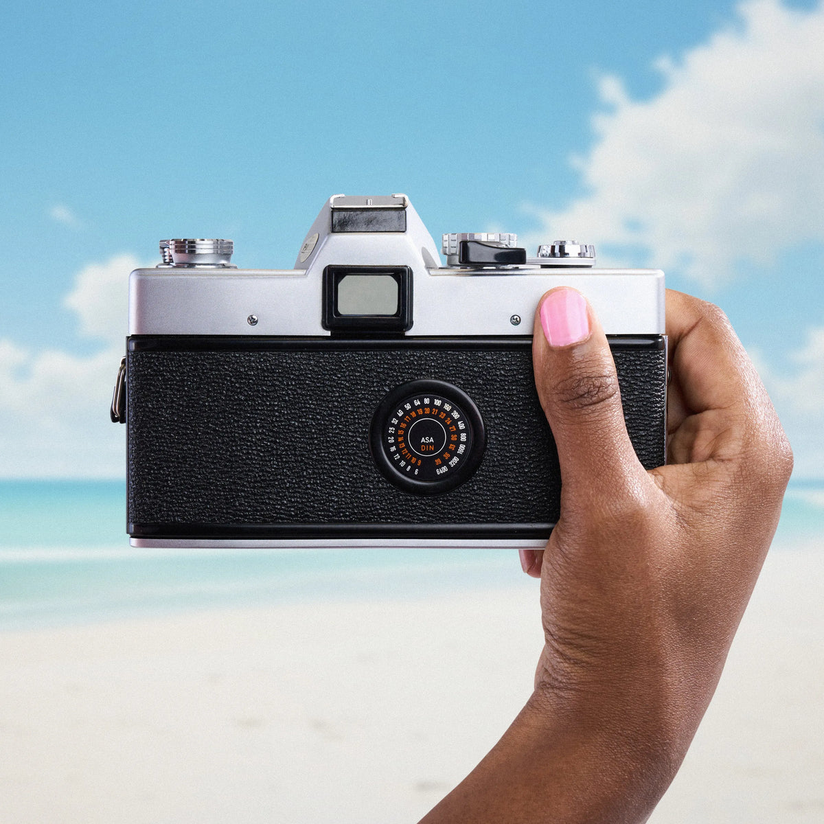 Hand holding a Minolta SRT 101 35mm film camera  with a beach and sky background
