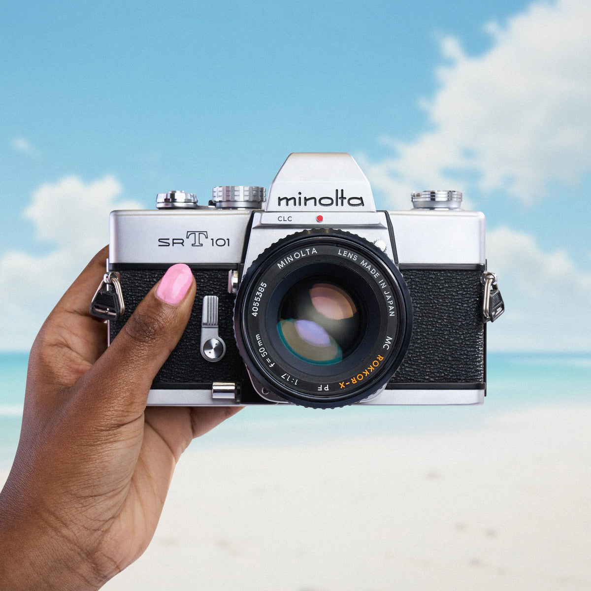 Minolta SRT 101 35mm film camera  held by a hand with a beach and sky background
