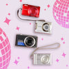 Four Mystery Digicam Blind Box cameras from different brands on a pink background with decorative elements.