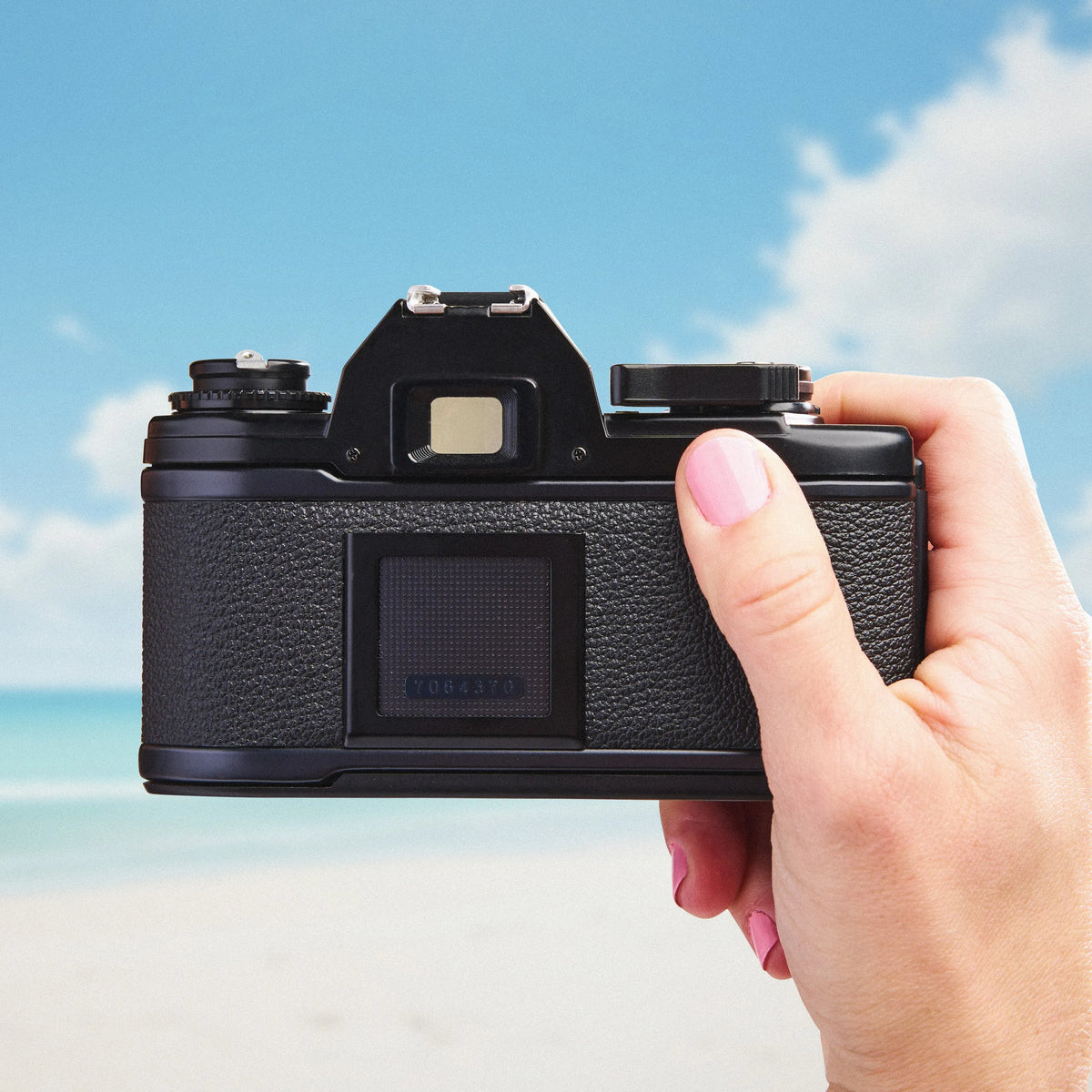 Hand holding a Nikon EM | 35mm Film Camera  against a beach background