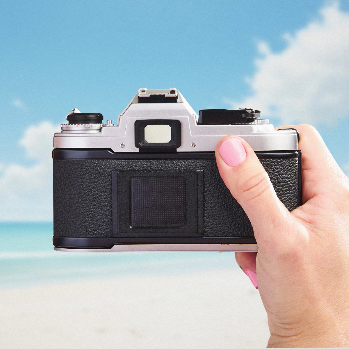 Hand holding a Nikon FG SLR film camera with a beach and sky background