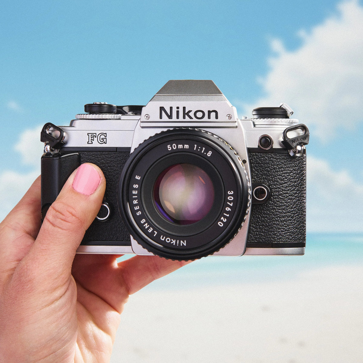 Hand holding a Nikon FG SLR film camera with a blue sky background