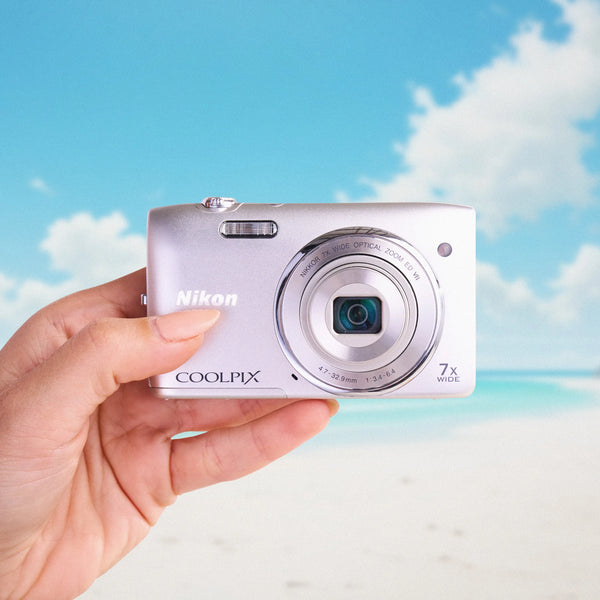 Hand holding a Nikon Coolpix s3500 with a beach and sky background