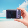 Hand holding a Nikon Coolpix s3500  with a beach and blue sky in the background