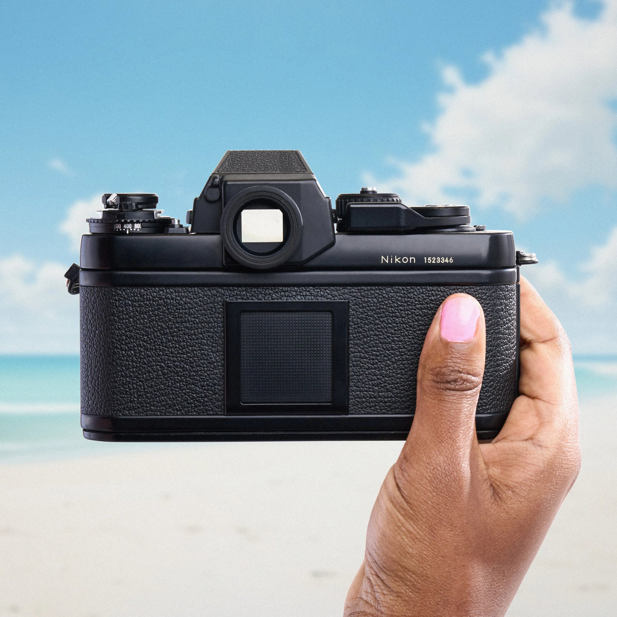 Hand holding a Nikon F3 35mm Film Camera with a beach and blue sky in the background