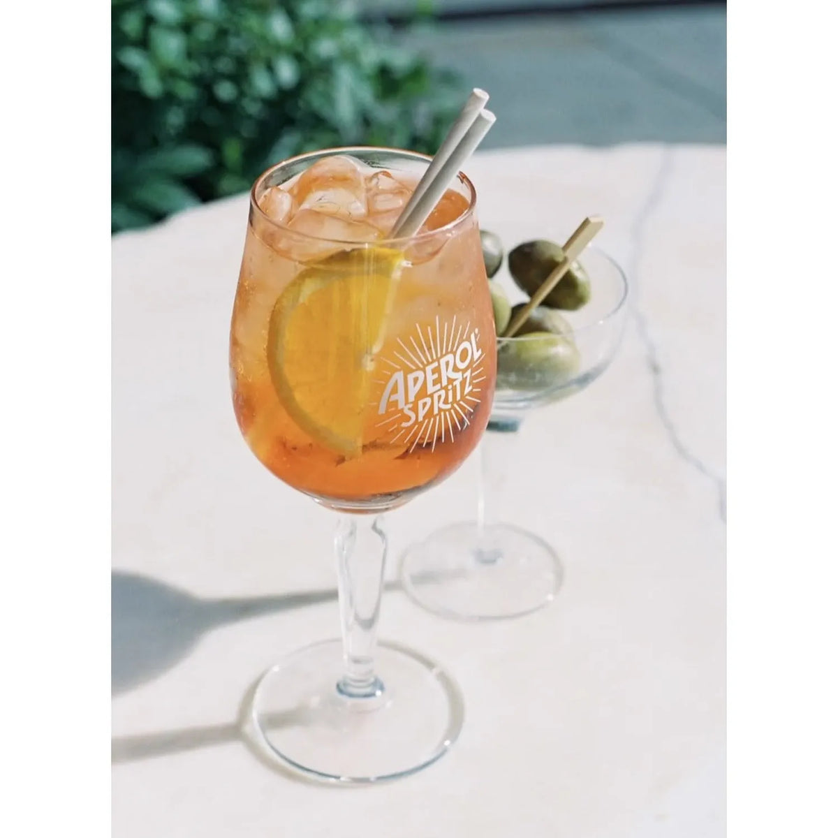 Glass of Aperol Spritz with a lemon slice and straw on a white surface. taken with a Olympus OM-1 | 35mm Film Camera