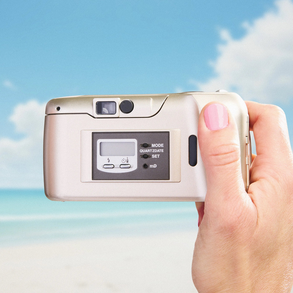 Hand holding a Olympus Stylus Epic 115 | 35mm Point and Shoot Film Camera with a beach background