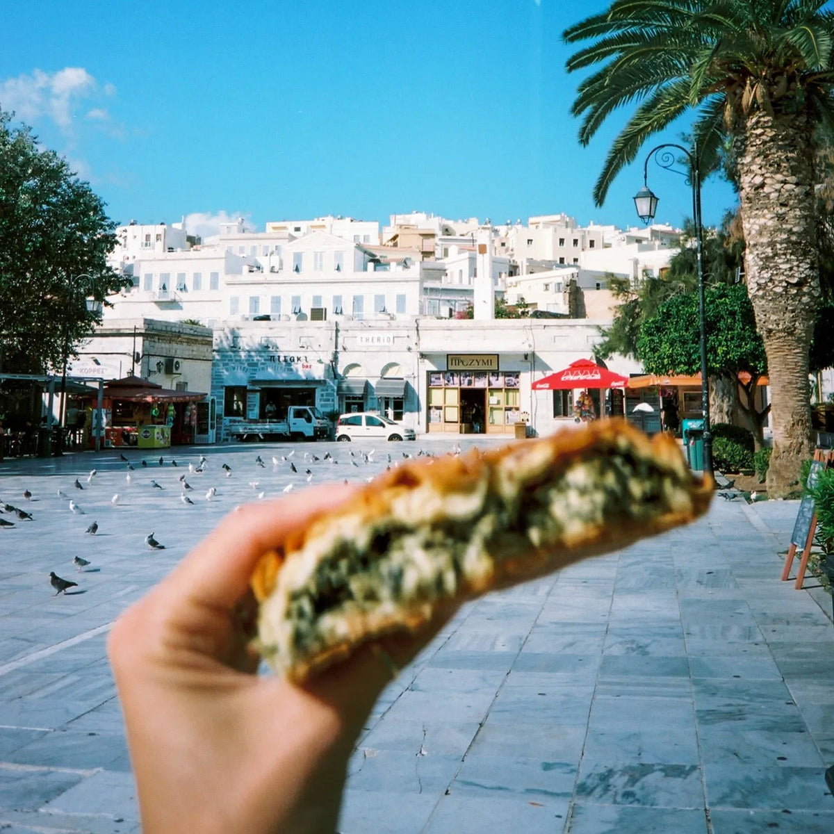 Person holding a pastry with a scenic background of buildings and palm trees taken with the Olympus OM-10 35mm Film Camera 