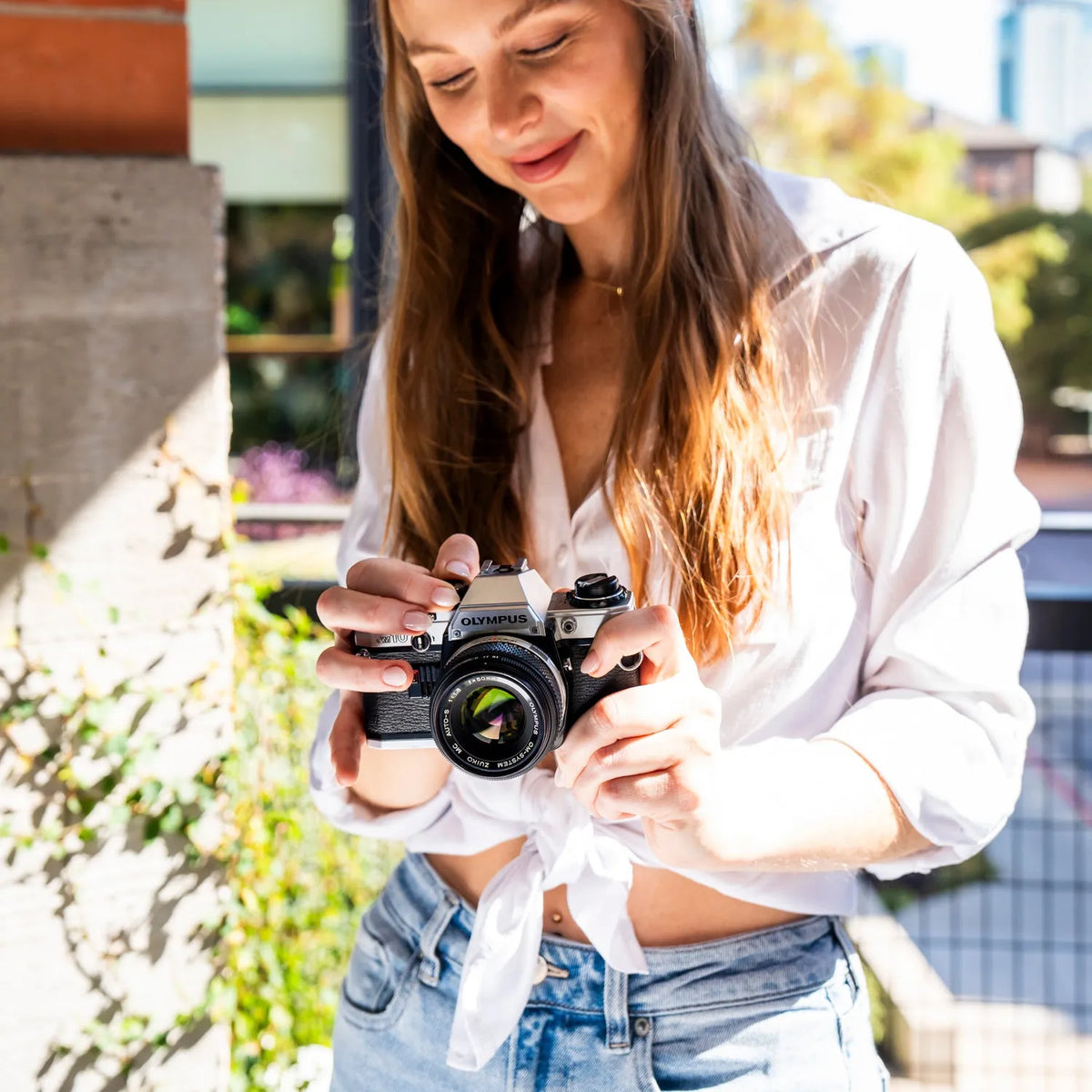 Woman holding a Olympus OM-10 35mm Film Camera outdoors with a blurred background