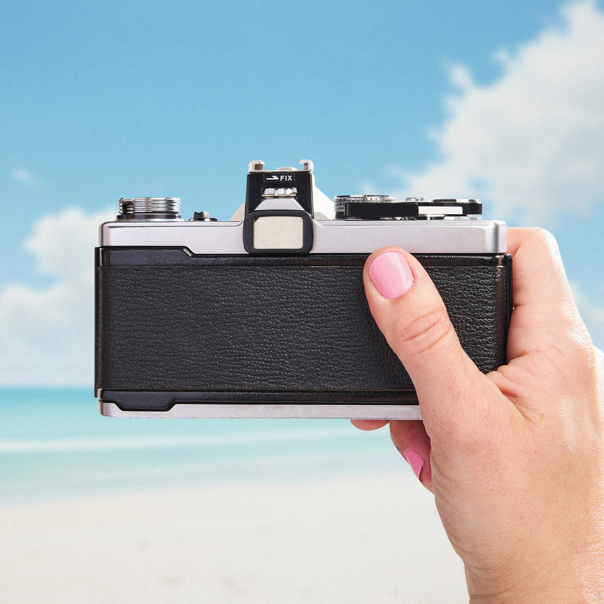 Hand holding a Olympus OM-1 35mm Film Camera with a beach and blue sky in the background