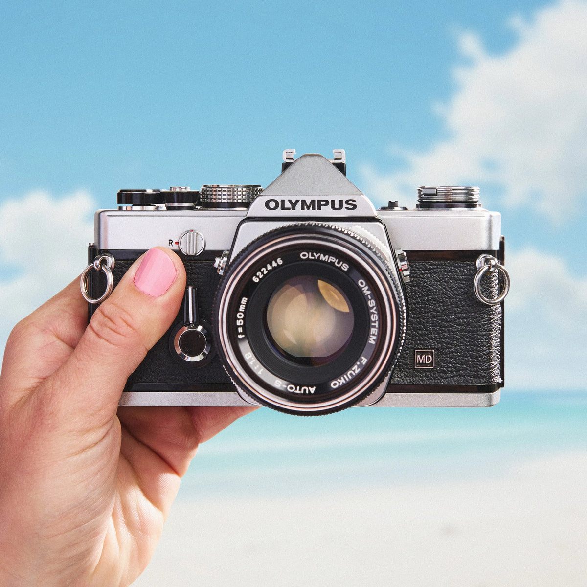 Hand holding an Olympus OM-1  35mm Film Camera against a blue sky background